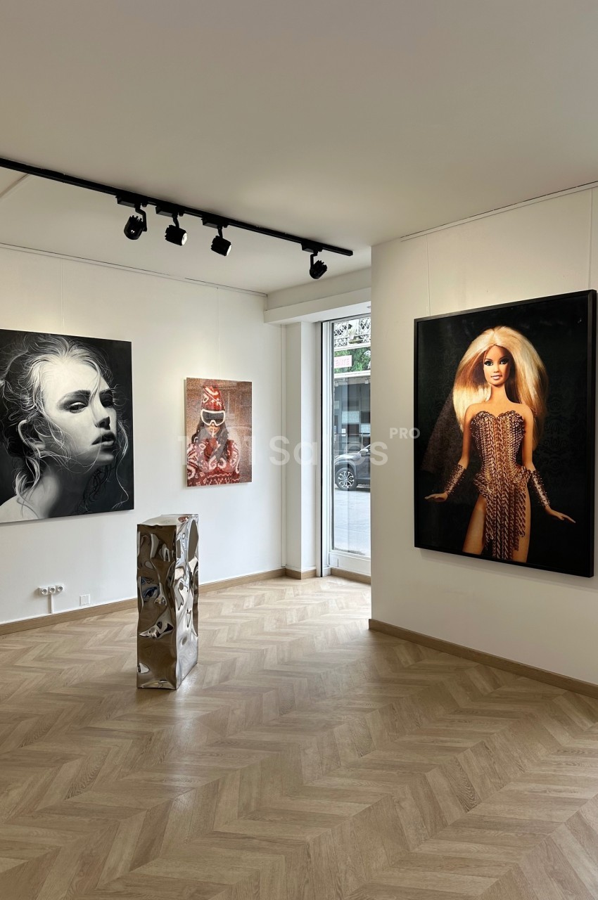 Vue d'une galerie d'art moderne avec des peintures accrochées aux murs et une sculpture métallique au centre.