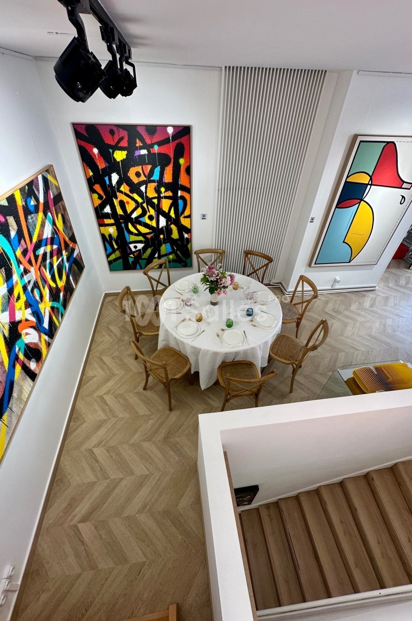 Vue d'une salle moderne avec une table ronde dressée, entourée de chaises en bois, et des tableaux abstraits accrochés aux…