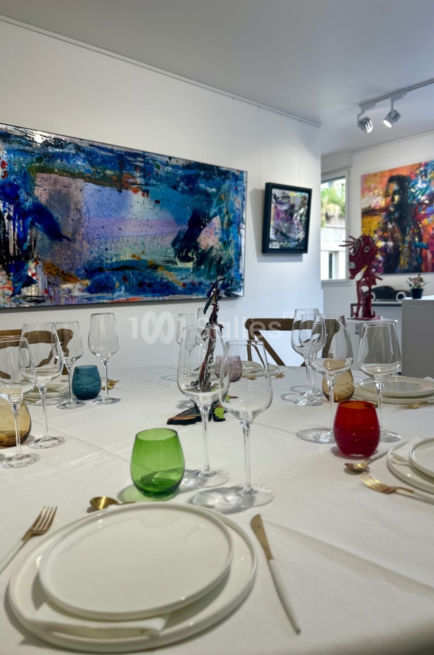 Table dressée avec vaisselle colorée dans une galerie d'art, entourée de peintures abstraites exposées sur les murs.