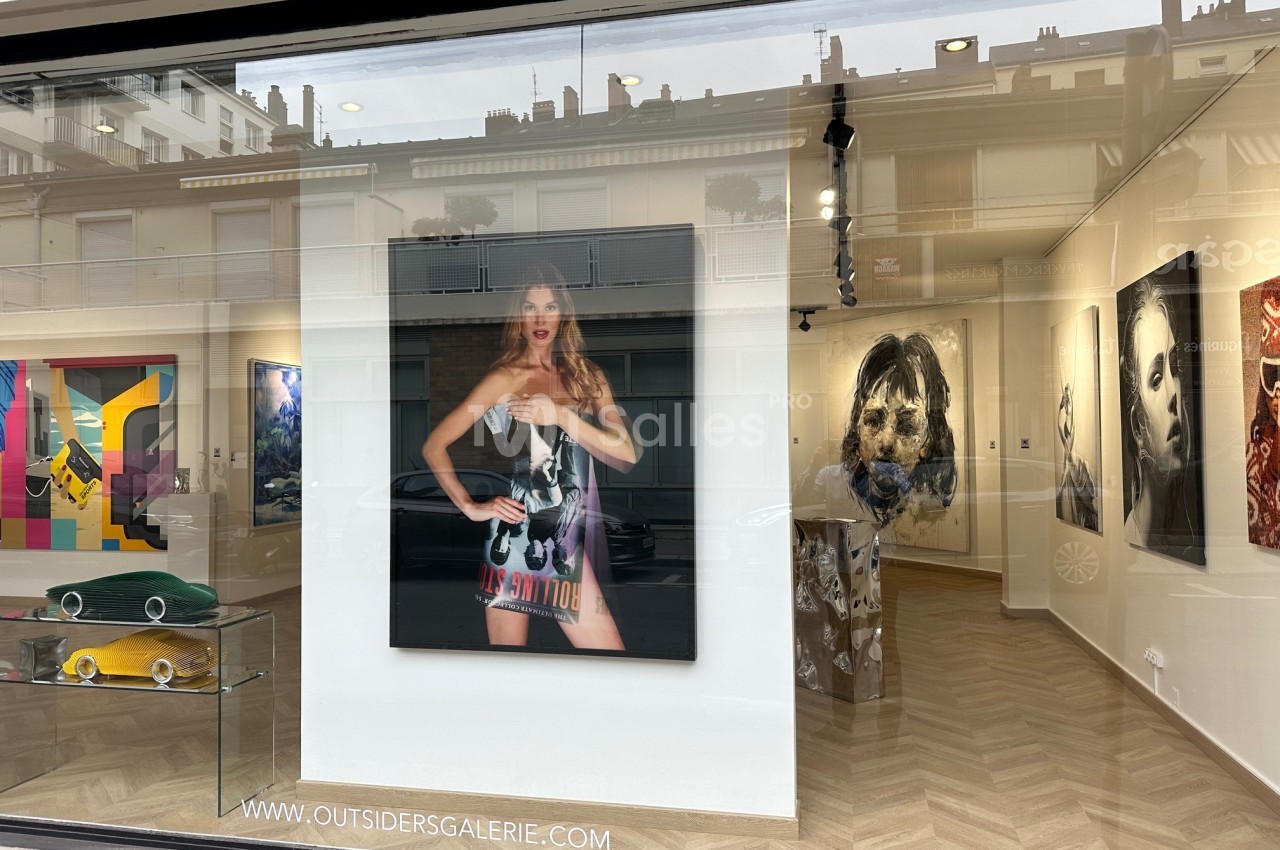 Vue d'une galerie d'art avec des œuvres contemporaines exposées, visibles à travers une vitrine en verre.