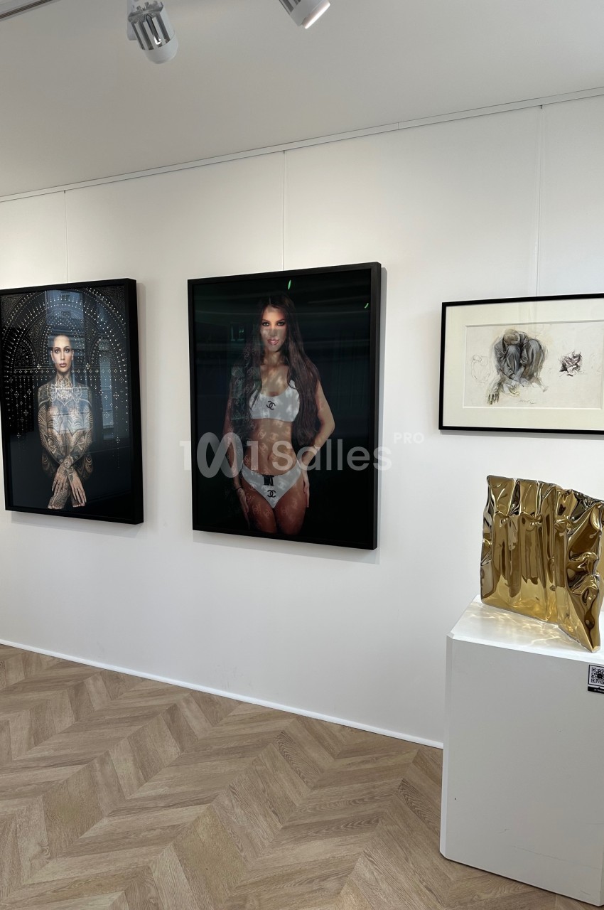 Vue d'une galerie d'art avec des photographies encadrées, un dessin et une sculpture dorée sur un socle.