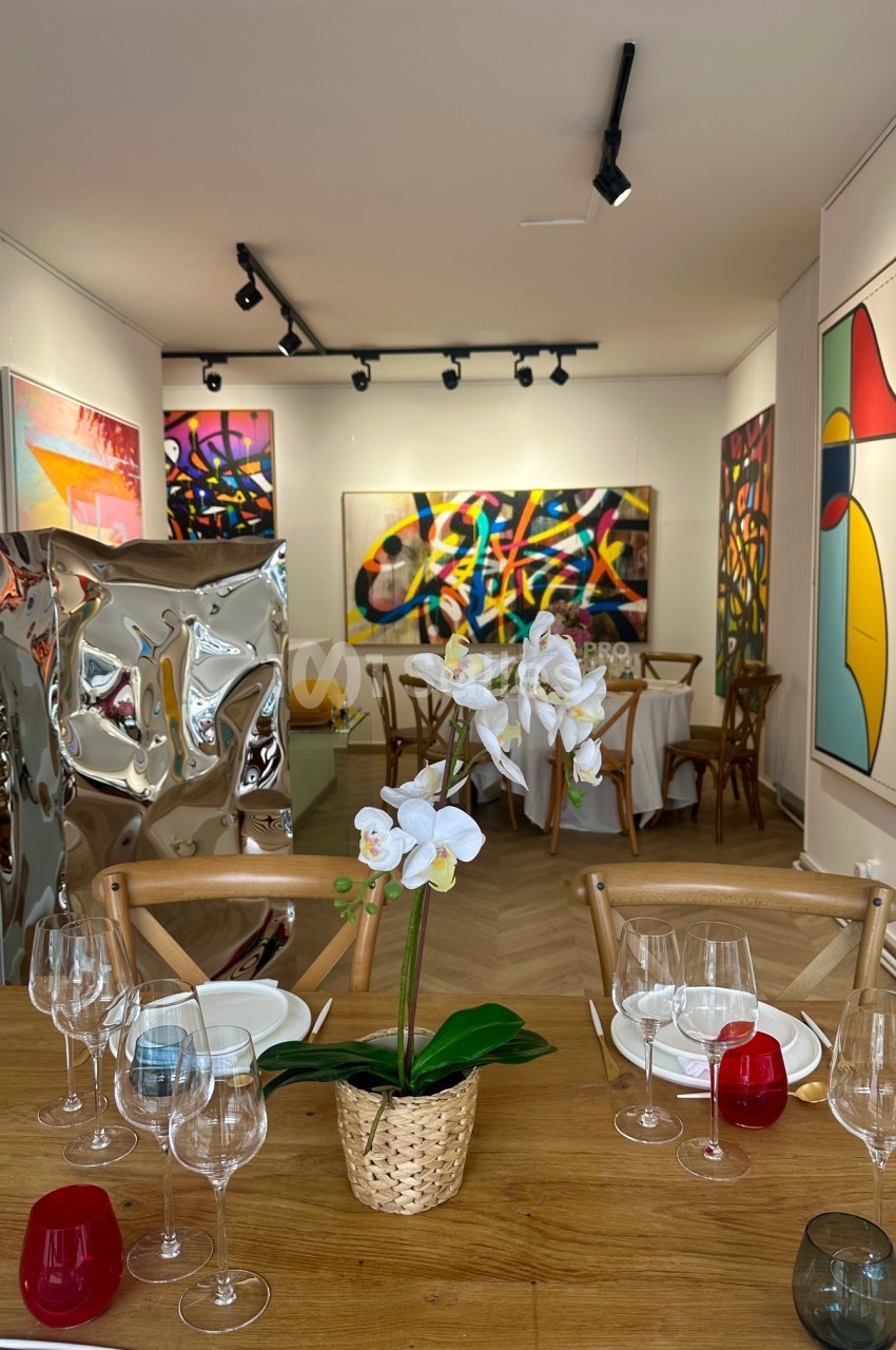 Salle d'exposition lumineuse avec des œuvres d'art colorées accrochées aux murs, table dressée au premier plan.