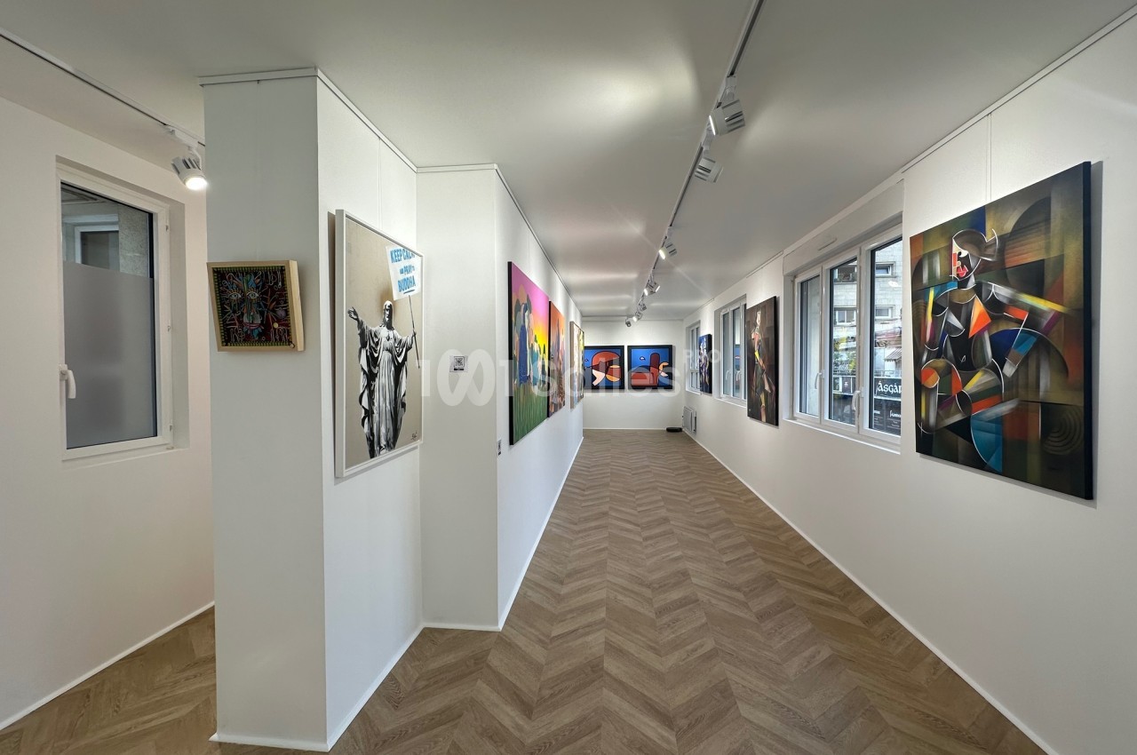 Vue intérieure d'une galerie d'art moderne avec des tableaux colorés accrochés sur des murs blancs et un sol en parquet.