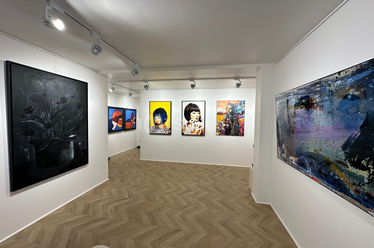 Vue d'une galerie d'art moderne avec des peintures colorées accrochées sur des murs blancs et un sol en parquet clair.