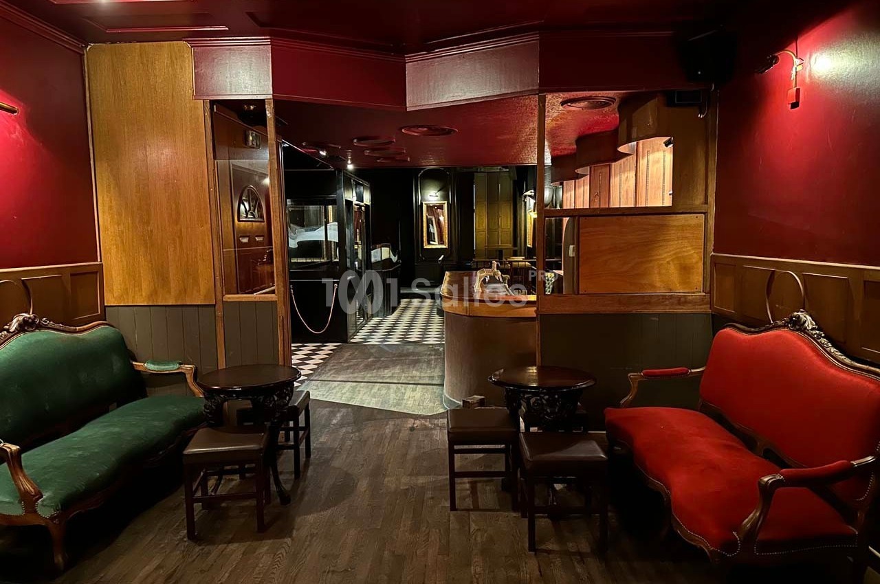 Intérieur d'un salon avec canapés rouges et verts, tables basses en bois, éclairage tamisé et sol en parquet.