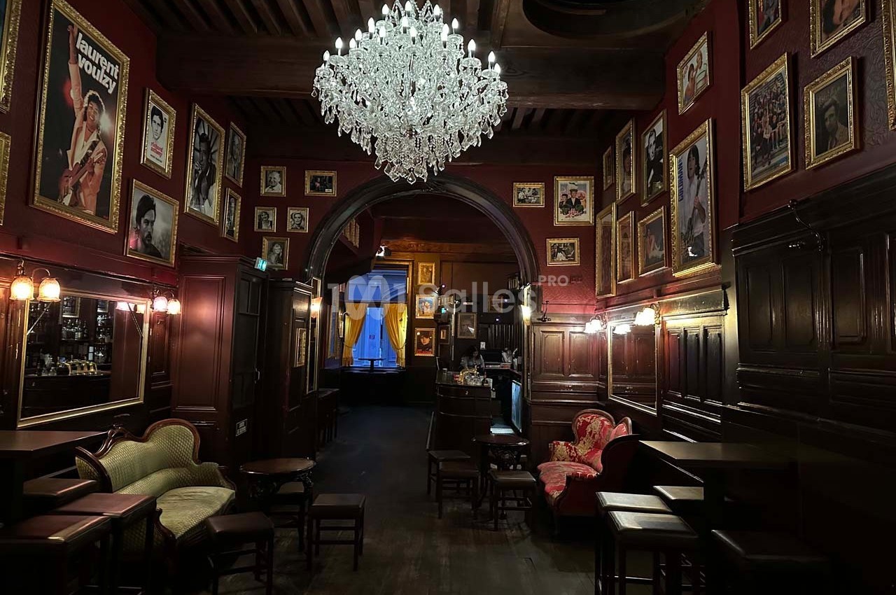 Salle de bar au décor vintage avec murs rouges ornés de cadres, lustre en cristal et mobilier ancien.