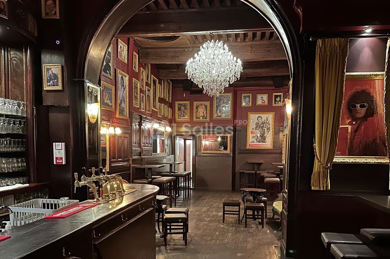 Intérieur d'un bar avec un lustre central, des murs ornés de cadres et un comptoir en bois sombre.