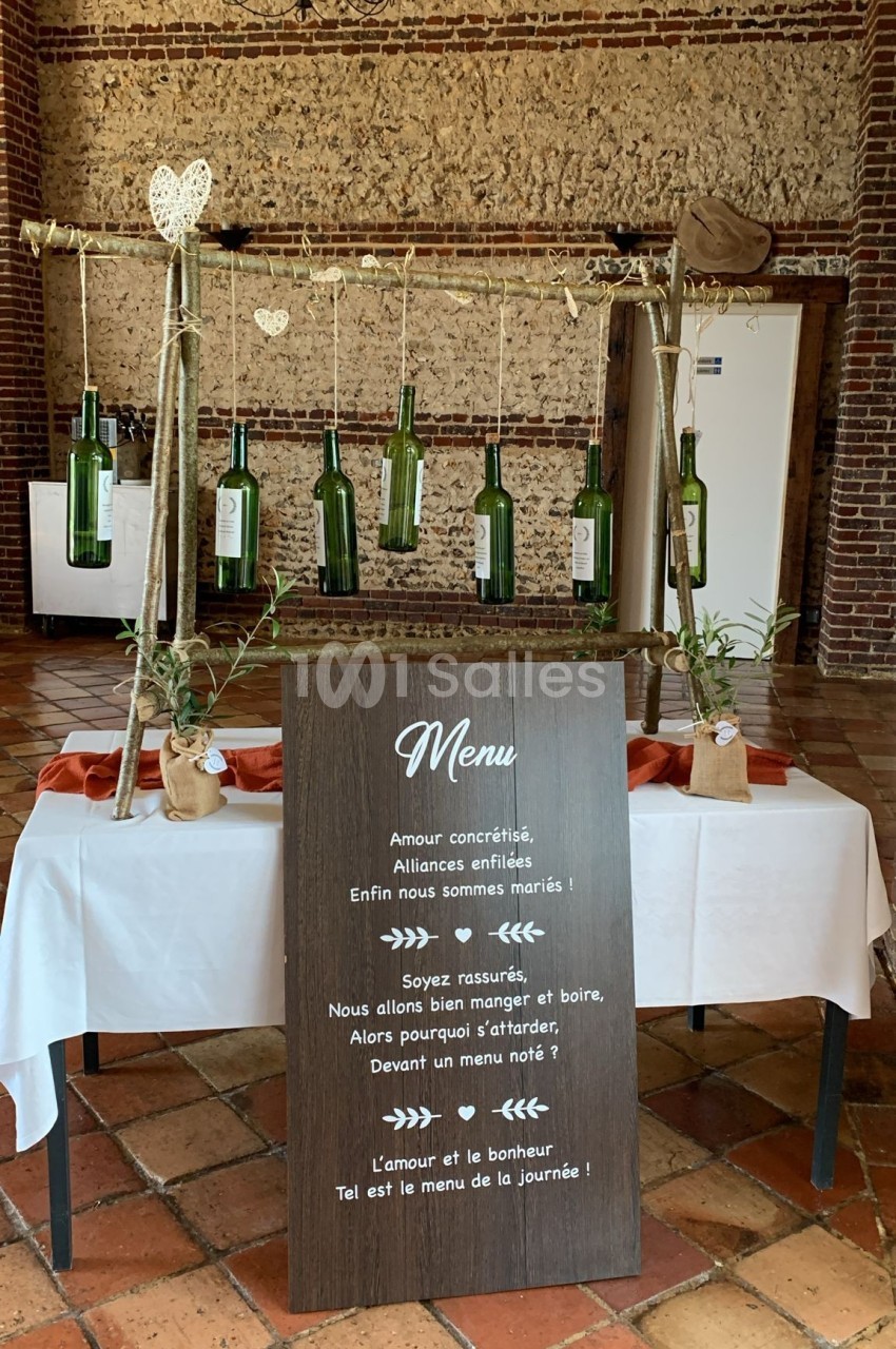 Décoration de mariage avec bouteilles suspendues et panneau en bois affichant un menu et un message romantique.