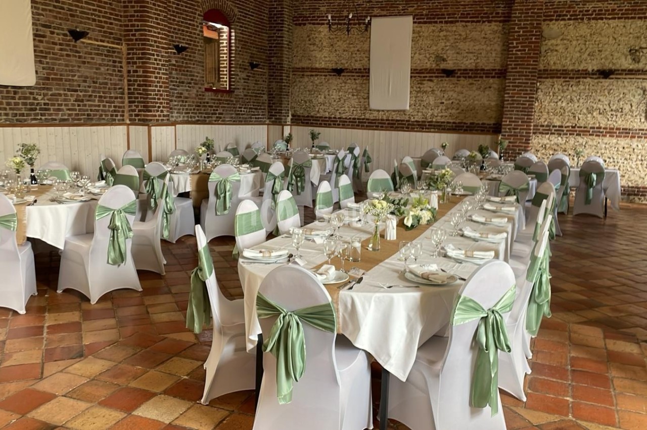 Salle de réception décorée avec des tables alignées, nappes blanches et chaises ornées de nœuds verts.