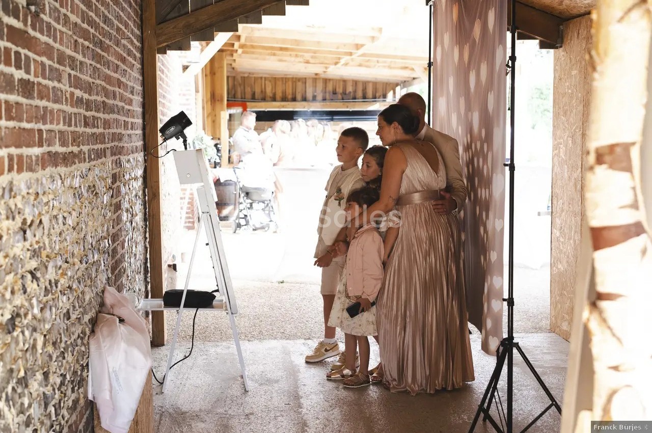 Une famille pose ensemble devant une borne photo dans un espace couvert en briques et bois.