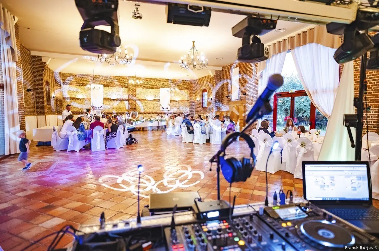 Vue d'une salle de réception avec des invités assis, éclairages décoratifs et matériel de DJ au premier plan.