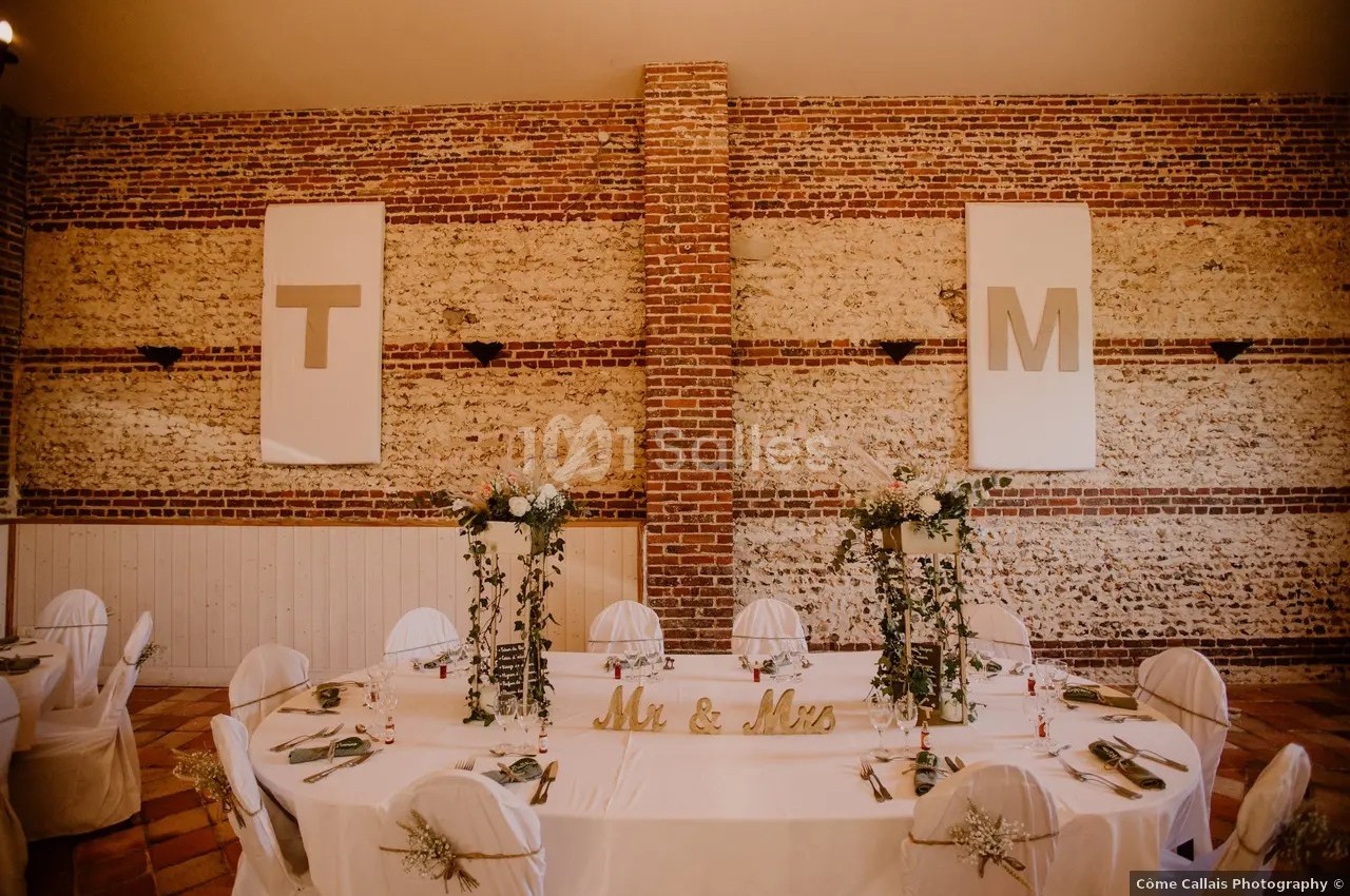 Salle de réception avec murs en briques, table décorée de fleurs et lettres ’T’ et ’M’ accrochées au mur.