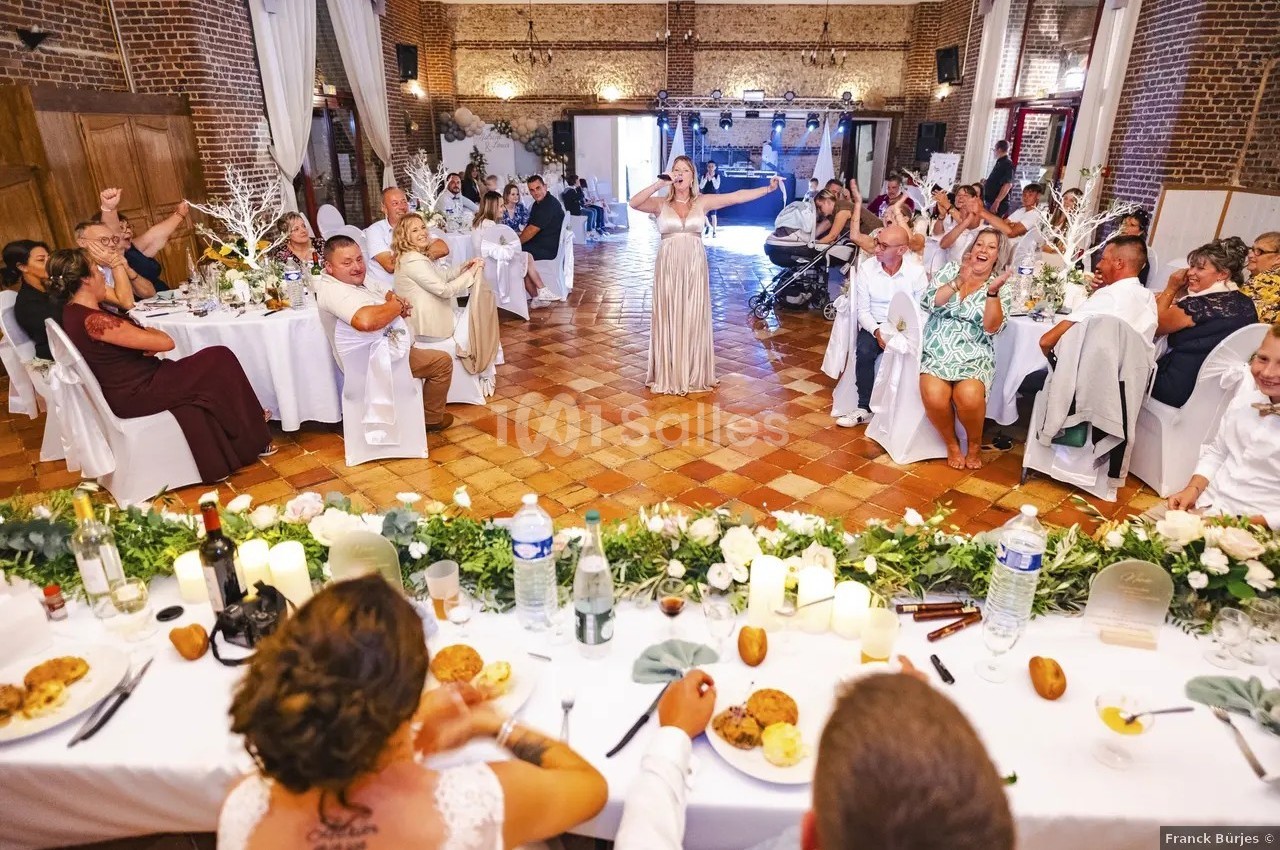 Une femme chante devant des invités assis à des tables décorées lors d'une réception dans une salle en briques.
