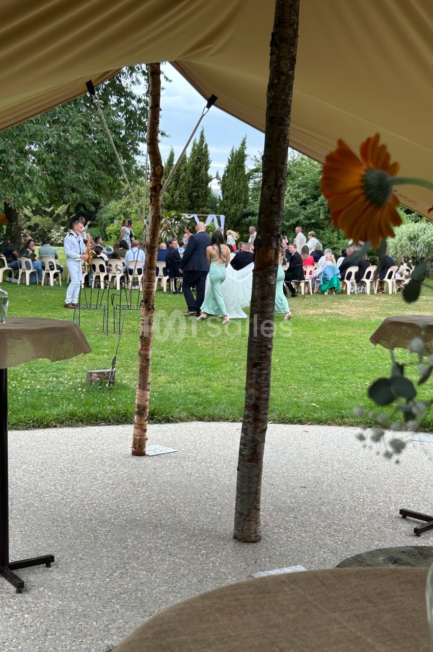 Vue depuis l'intérieur d'une tente sur un mariage en plein air avec des invités assis et des arbres en arrière-plan.