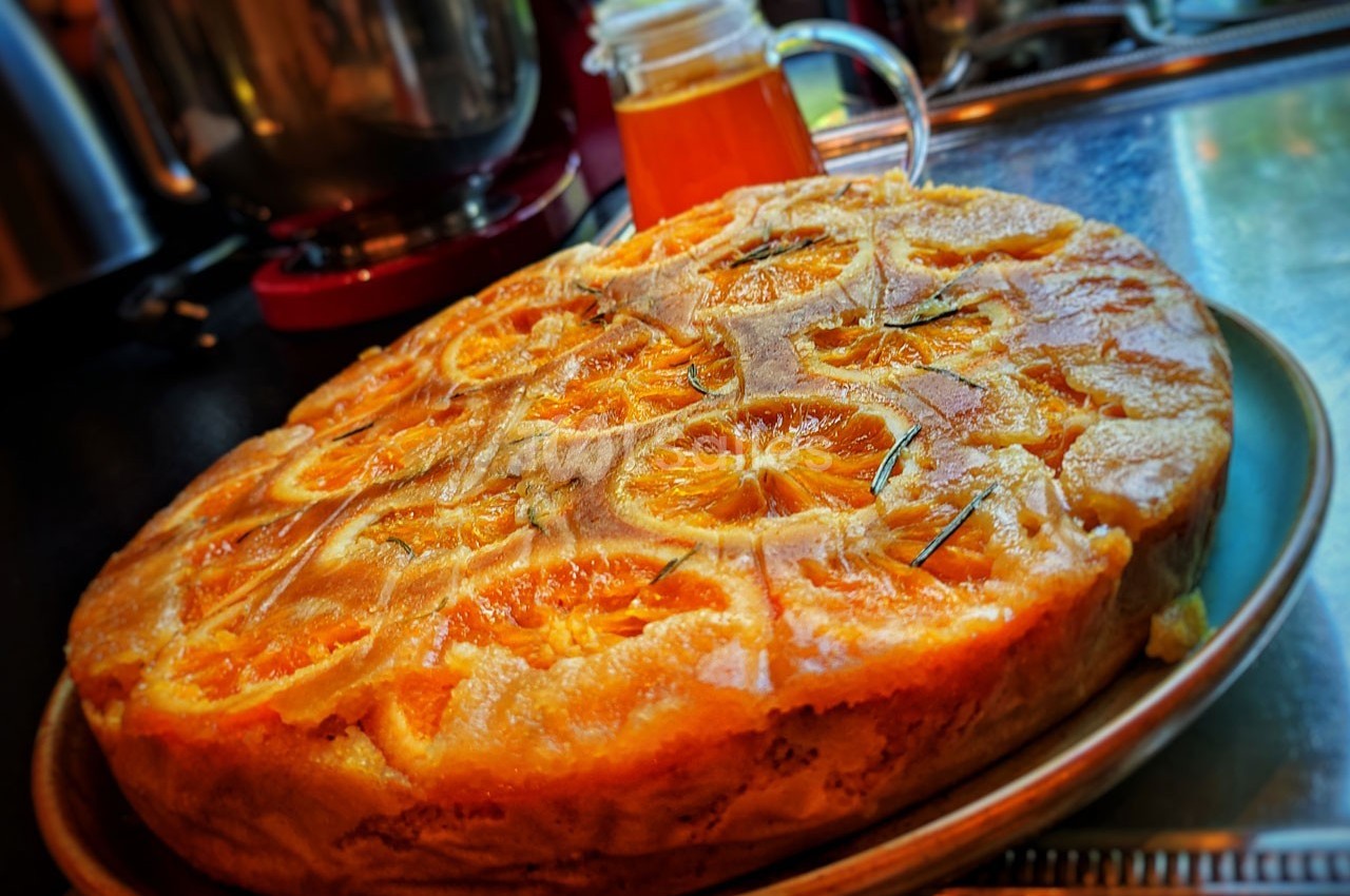 Gâteau renversé aux oranges caramélisées posé sur une assiette dans une cuisine avec un pot de miel en arrière-plan.