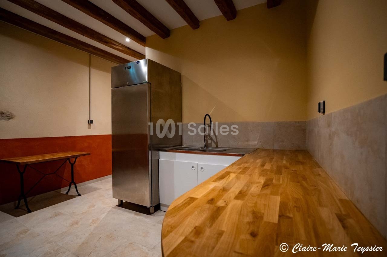Cuisine minimaliste avec plan de travail en bois, évier inox, réfrigérateur et table pliante sur sol carrelé.