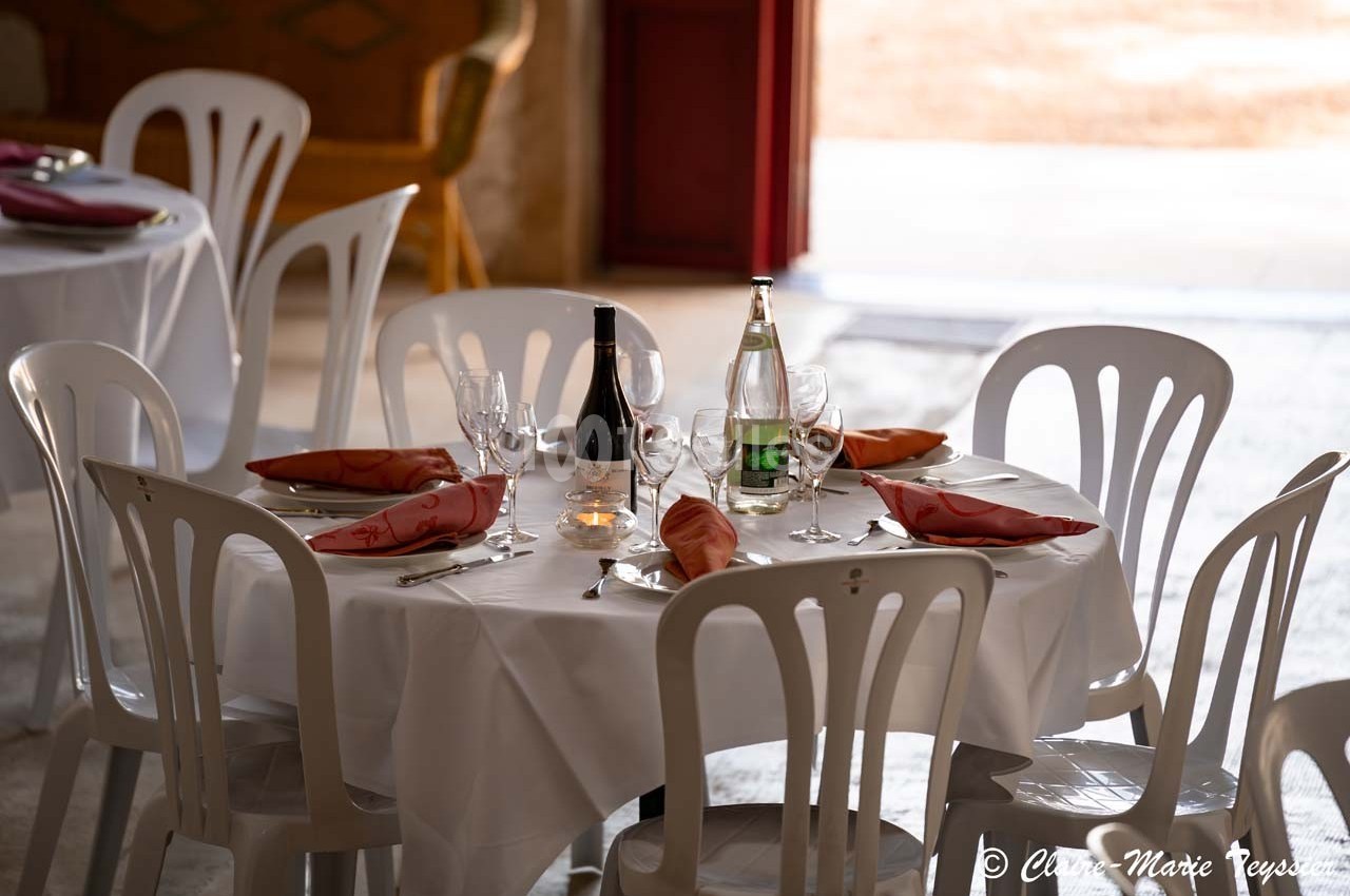 Table ronde dressée avec nappes blanches, chaises en plastique, verres, serviettes rouges, bouteille de vin et eau.