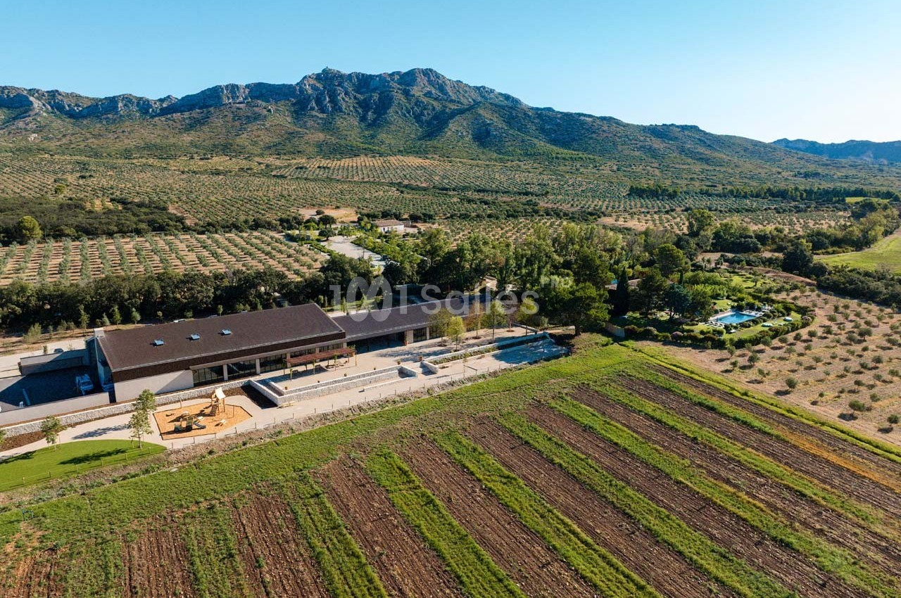 Vue aérienne d'un domaine agricole avec champs cultivés, bâtiment moderne et collines en arrière-plan.