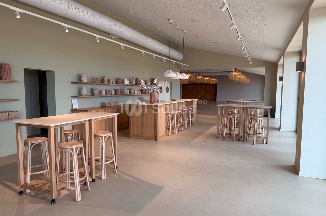 Salle lumineuse avec tables hautes en bois, tabourets et étagères décorées de vases dans un style épuré.