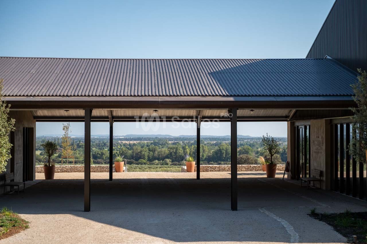 Vue d'un bâtiment moderne avec toit en métal, ouvert sur un paysage rural avec des collines et des arbres à l'horizon.