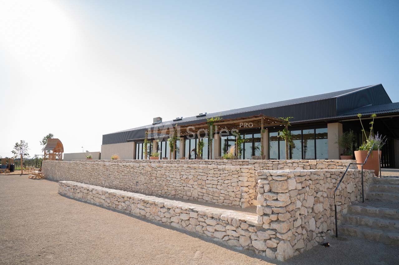 Bâtiment moderne avec terrasse ombragée, entouré de murs en pierre et situé dans un espace extérieur dégagé.