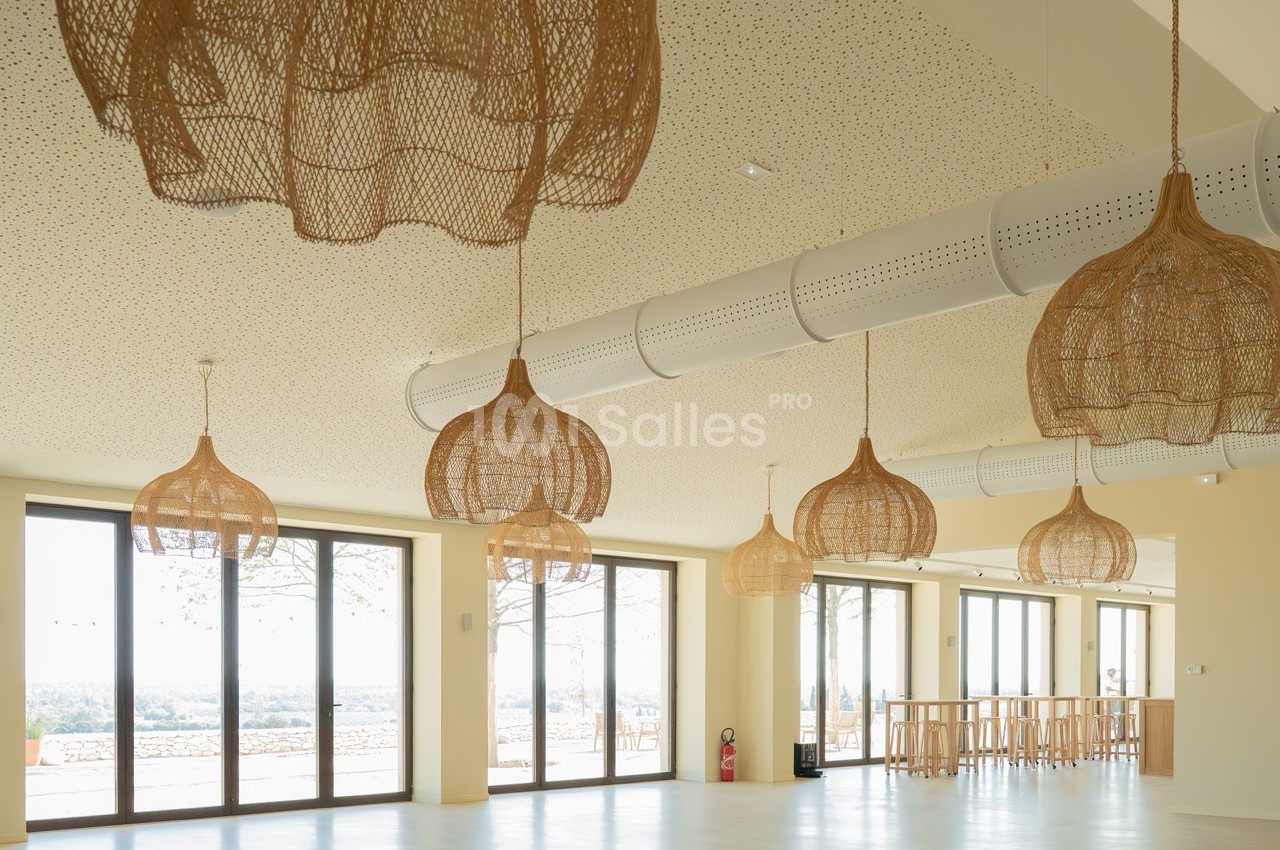 Suspensions en rotin dans une grande salle lumineuse avec baies vitrées donnant sur un paysage extérieur.