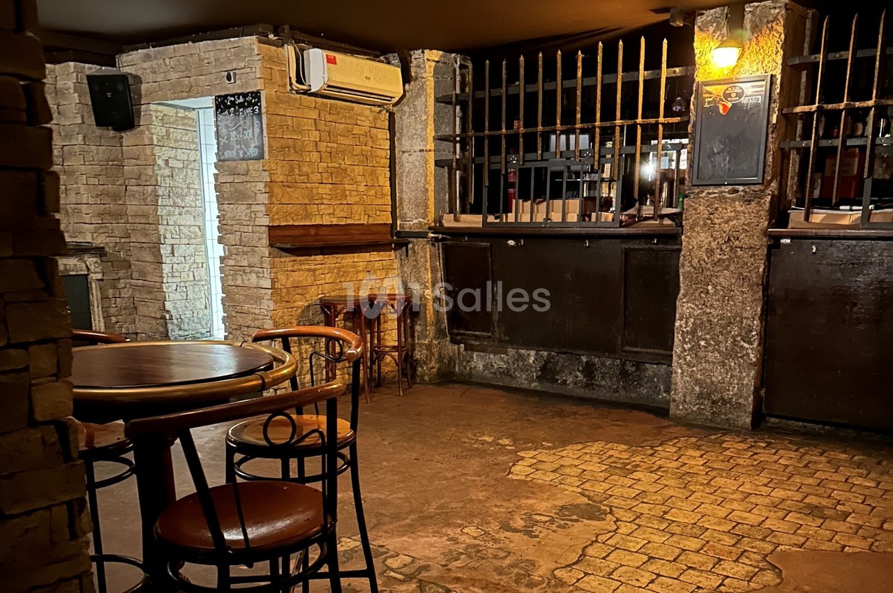 Salle intérieure avec murs en pierre, tables et chaises en bois, éclairage tamisé et comptoir avec grille métallique.
