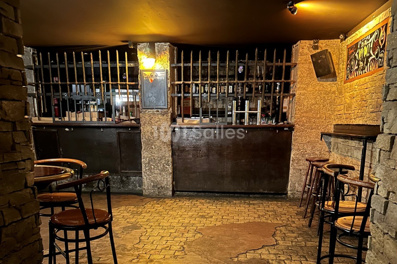 Intérieur d'un bar avec comptoir en bois, tabourets hauts, murs en pierre et éclairage tamisé.