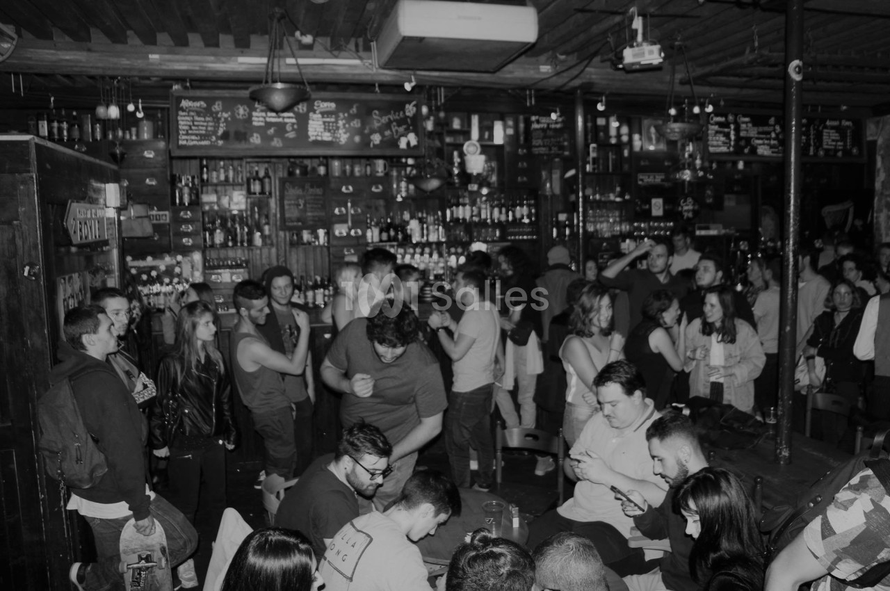 Groupe de personnes dans un bar animé, discutant et socialisant dans une ambiance conviviale en noir et blanc.