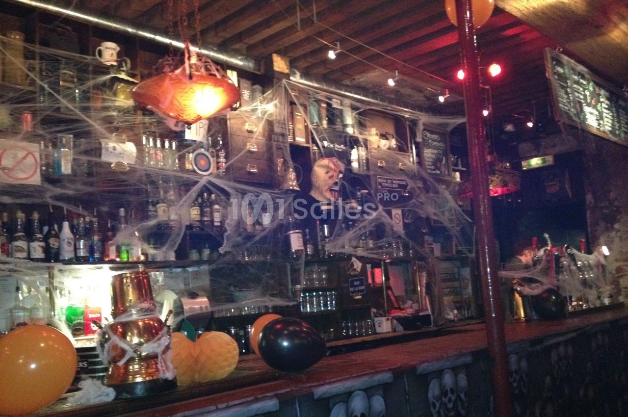 Bar décoré pour Halloween avec des toiles d'araignée, des ballons orange et noirs, et des bouteilles alignées sur des…
