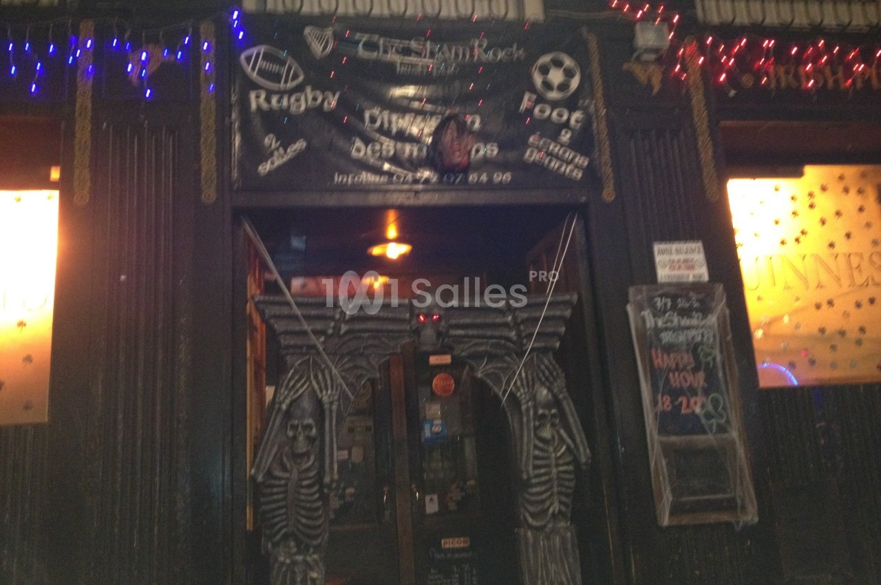Entrée d'un bar décoré avec des squelettes et des lumières, avec une bannière annonçant des événements sportifs.