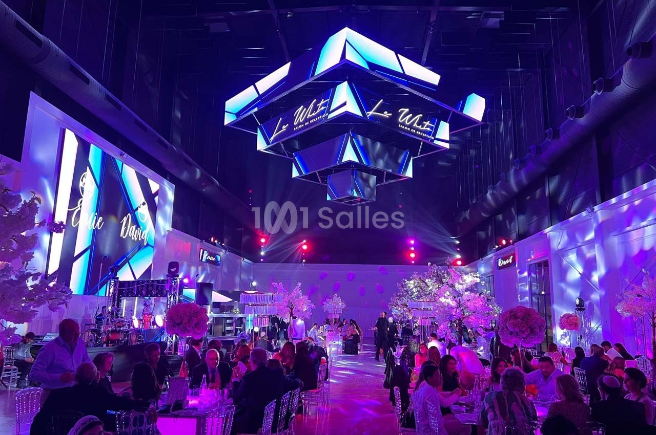 Salle de réception illuminée en violet avec des invités assis, des tables décorées et un éclairage suspendu moderne.