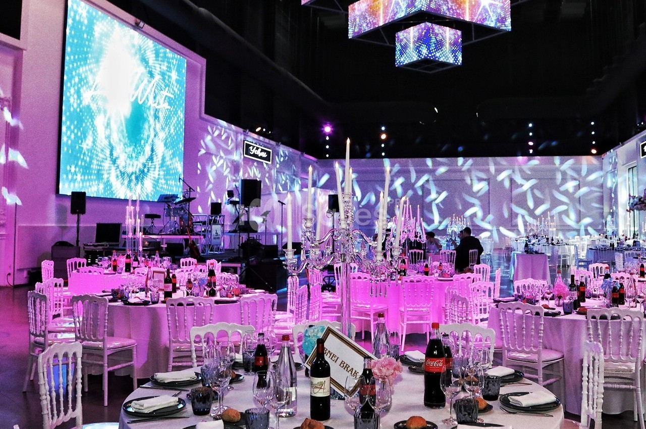 Salle de réception décorée avec des tables dressées, des chandeliers et des éclairages colorés.
