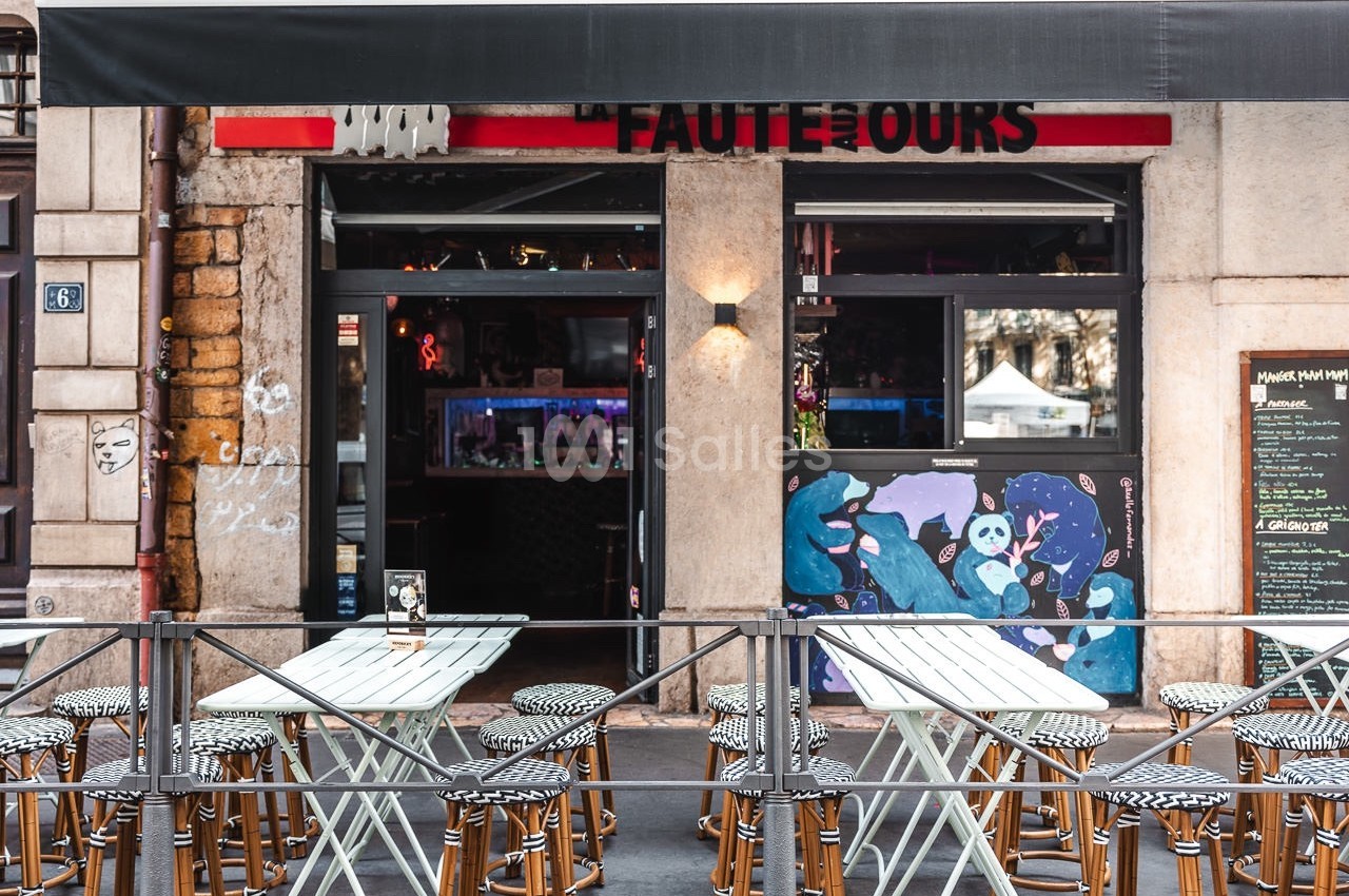 Terrasse avec tables et chaises devant un café au store noir, façade ornée de graffitis colorés.