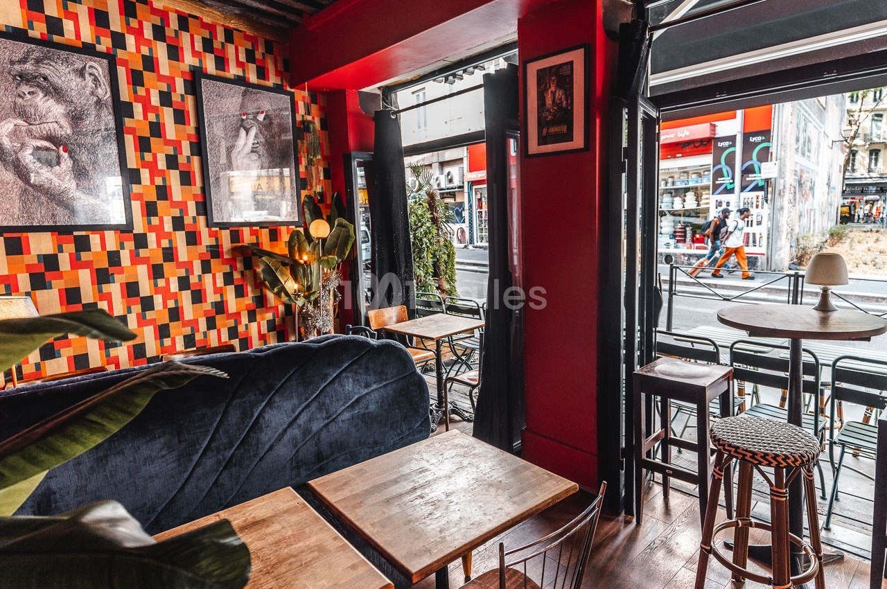Intérieur d'un café avec mobilier en bois, banquette bleue, murs colorés et vue sur une rue animée à travers la vitrine.