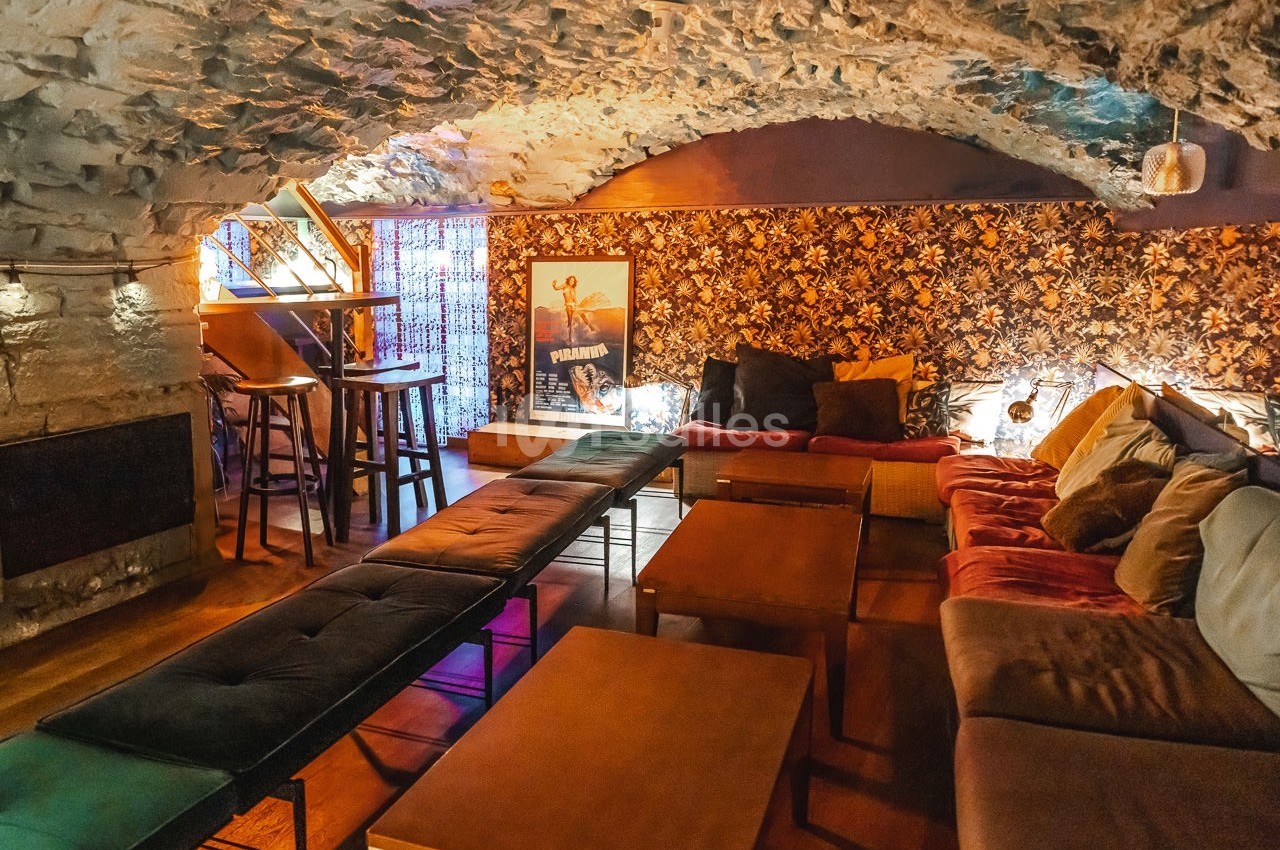 Salle voûtée avec murs en pierre, décor chaleureux, canapés, tables basses et éclairage tamisé.