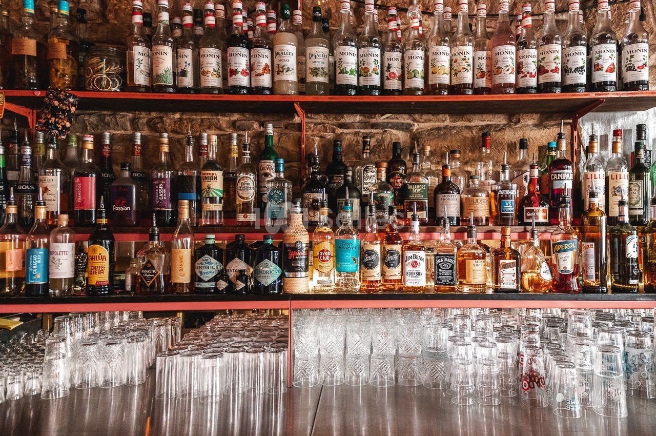 Étagères remplies de bouteilles d'alcool variées au-dessus d'un comptoir avec des verres alignés.