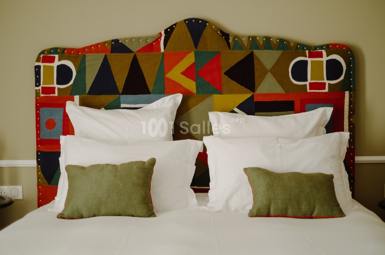 Lit avec tête de lit colorée à motifs géométriques, deux oreillers blancs et deux coussins verts.