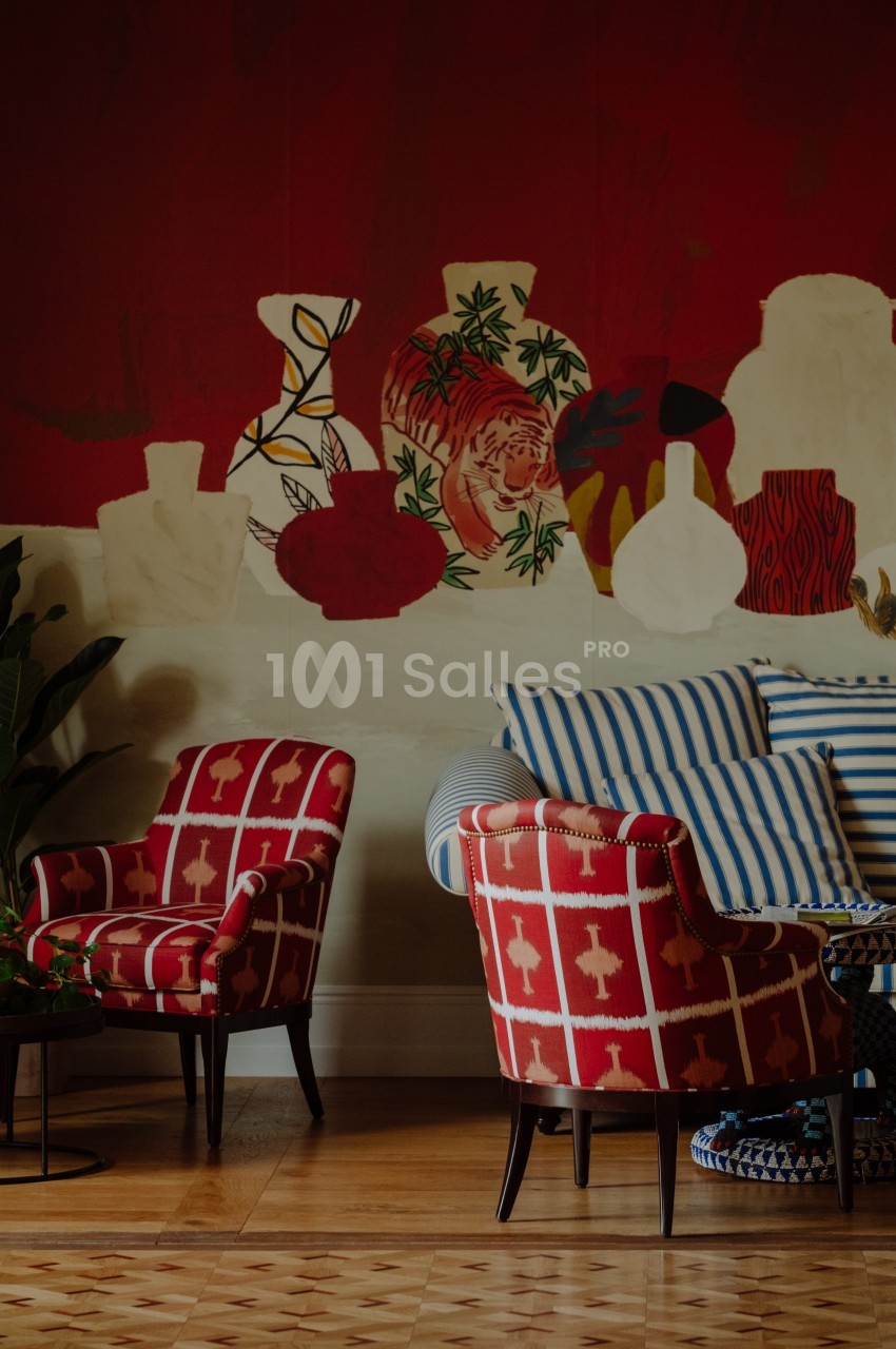 Deux fauteuils rouges à motifs blancs et un canapé rayé bleu et blanc devant un mur rouge décoré de vases peints.