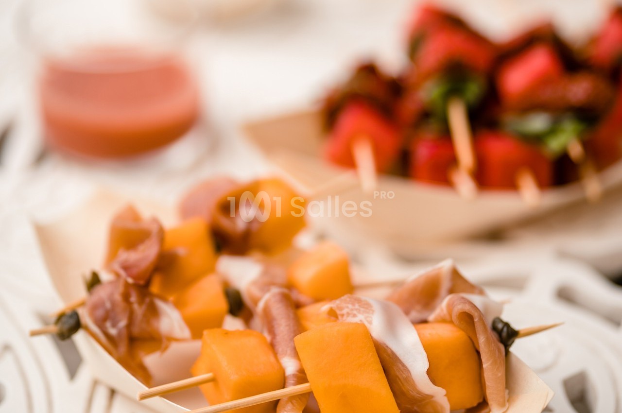 Brochettes de melon, jambon cru et mozzarella au premier plan, fraises en brochettes floues à l'arrière-plan.