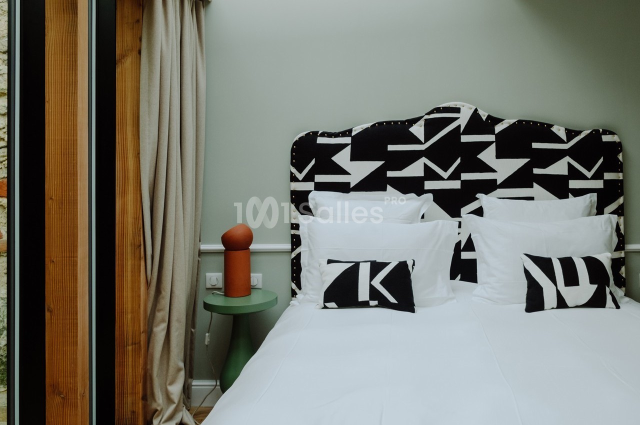 Lit double avec tête de lit noire et blanche à motifs géométriques, deux coussins assortis et table de chevet verte.