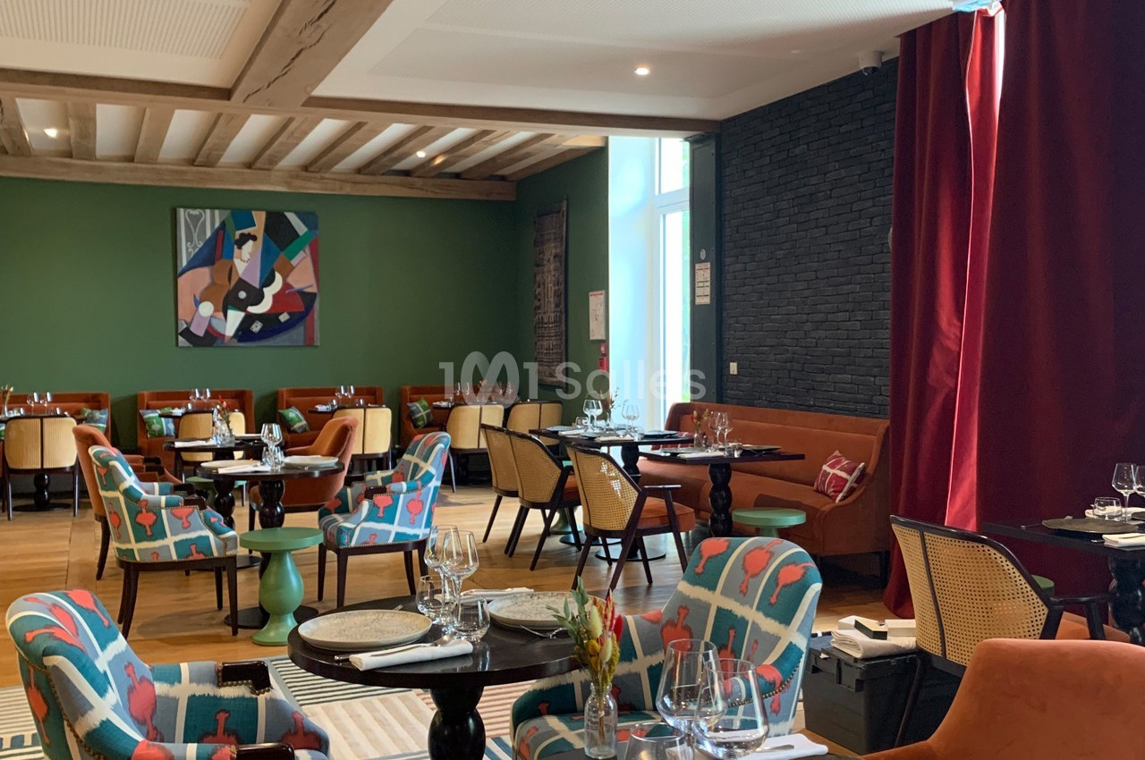 Salle de restaurant lumineuse avec des tables dressées, des fauteuils colorés et une décoration moderne.