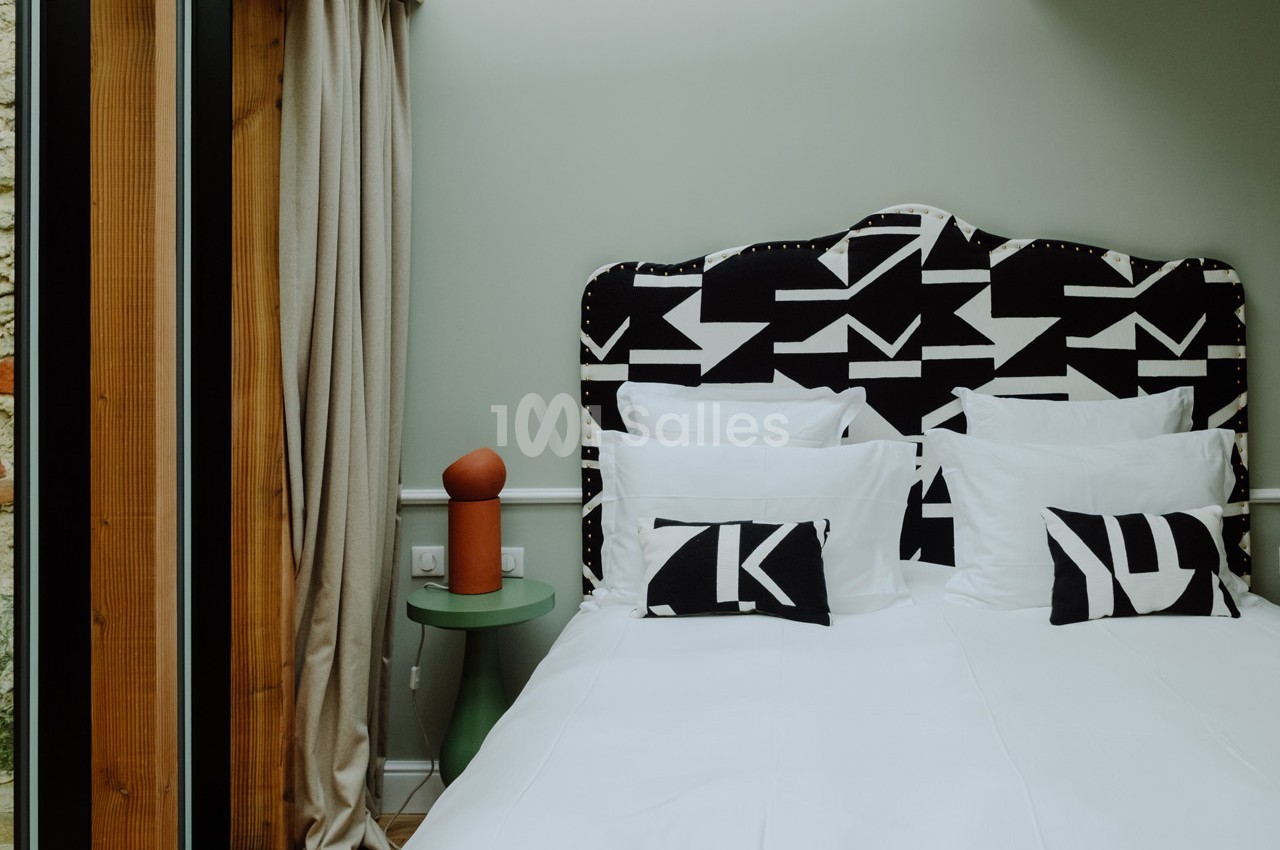 Lit double avec tête de lit à motifs géométriques noirs et blancs, draps blancs et coussins assortis, dans une chambre…