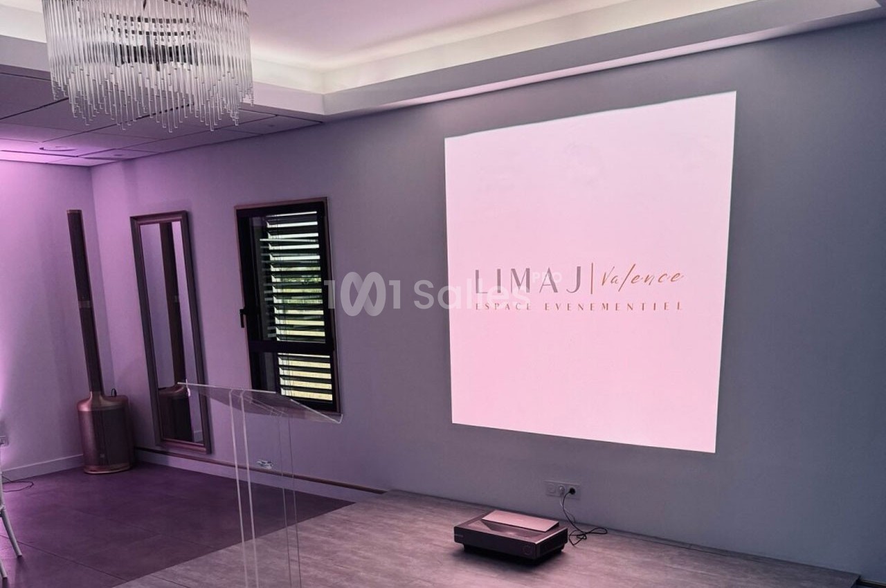 Salle moderne avec écran de projection affichant ’Limaj Valence’, éclairage tamisé et mobilier minimaliste.