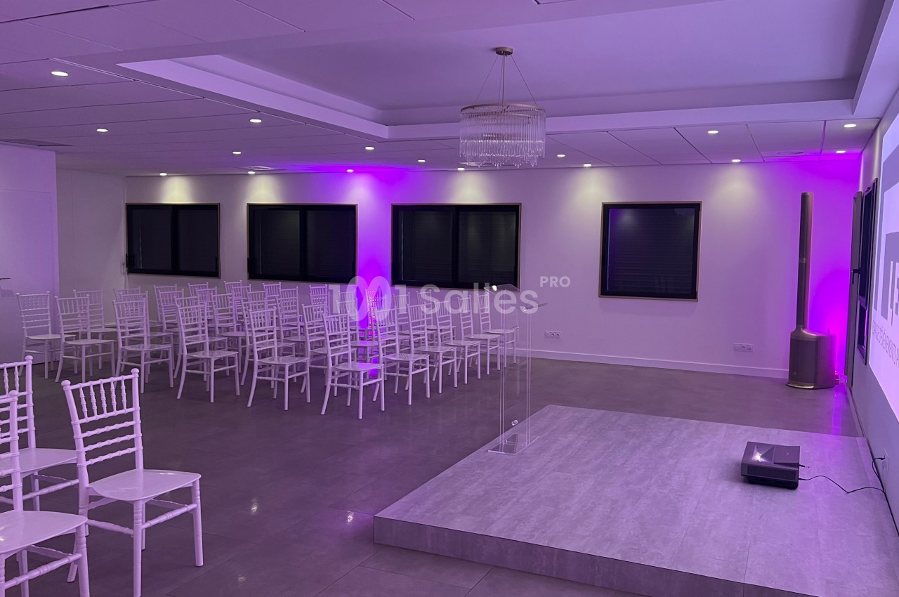 Salle de conférence moderne avec chaises blanches alignées, estrade et éclairage violet.