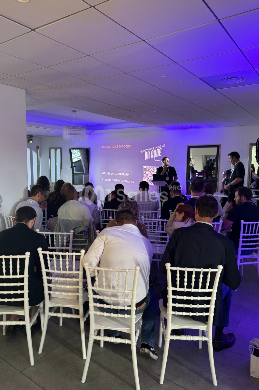Des personnes assises assistent à une présentation dans une salle éclairée par des lumières violettes.