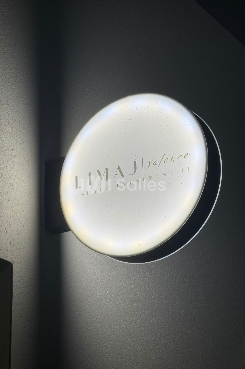 Enseigne lumineuse ronde indiquant ’Limaji Valence, espace événementiel’ fixée sur un mur sombre.
