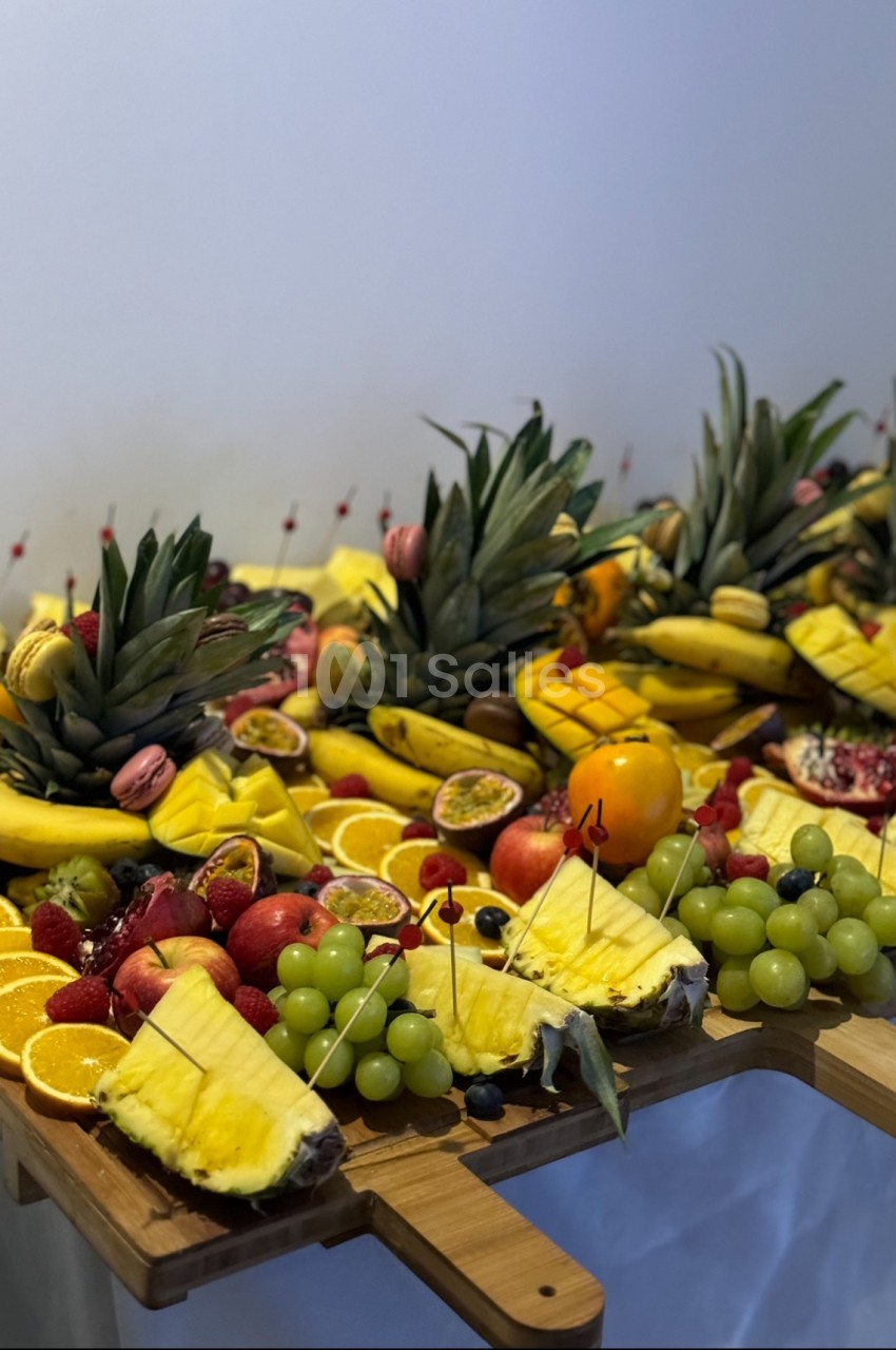 Plateau de fruits variés avec ananas, oranges, raisins, bananes, fruits de la passion et grenades sur une table en bois.