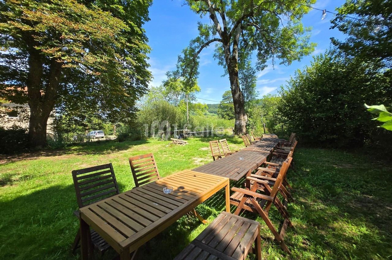 Tables et chaises en bois disposées en extérieur dans un jardin verdoyant sous un ciel bleu.