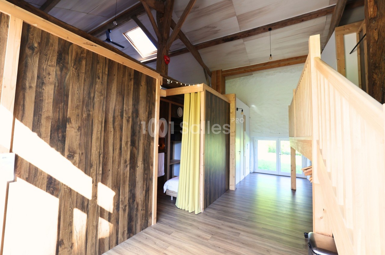 Intérieur lumineux avec murs en bois, escalier en bois clair et plafond avec poutres apparentes.
